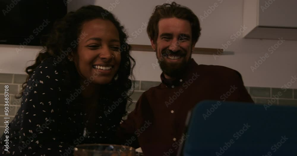 Happy couple sitting in kitchen laughing and using tablet