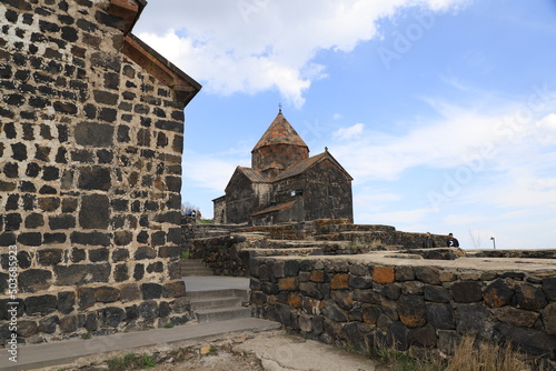 Churches and walls of the ancient Sevanavank monastery on Lake Sevan in Armenia - against a blue sky with white clouds.