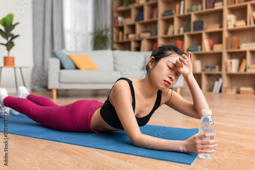 Exhausted asian lady wiping sweat from her forehead, feeling tired after training at home, lying on yoga mat