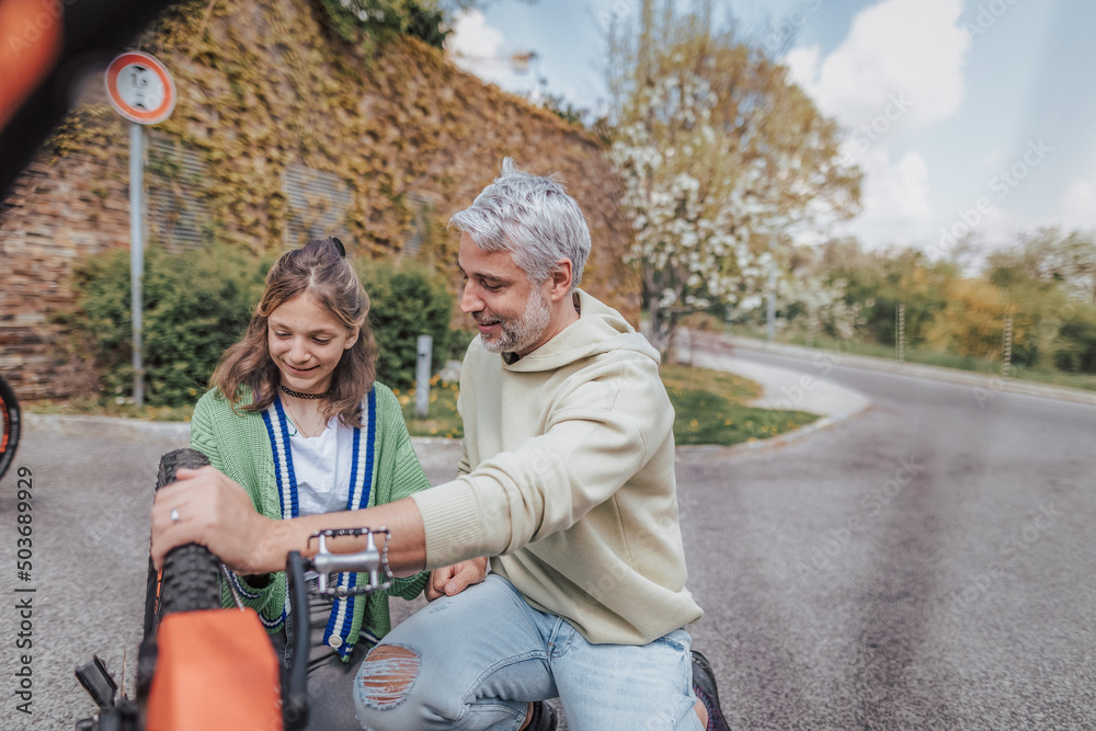Happy father with teenage daughter repairing bicycle in street in town. Happy father with teenage daughter repairing bicycle in street in town.