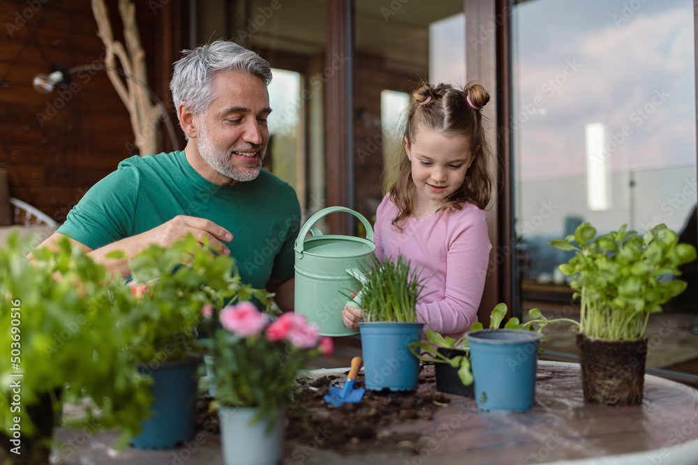 Little daughter helping father to plant and water flowers, home gardening concept