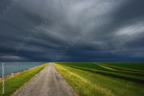 Strada rurale con campi di erba verde e cielo con temporale e nuvole in arrivo