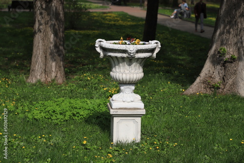 White flowerpot with flowers in the park on a spring day.