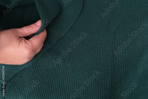 close-up of female hand touches knitted jersey, embossed canvas, green wool yarn, knitted texture, concept of warm things for cold weather, check quality, fashionable clothes, clothing production