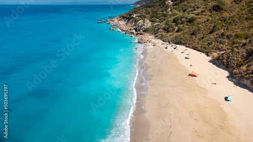 Aerial view of beautiful sandy beach with sunshades and soft turquoise ocean wave. Tropical sea in summer season on Megali Petra beach on Lefkada island.