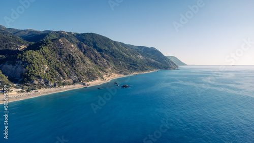 Aerial view of beautiful sandy beach with sunshades and soft turquoise ocean wave. Tropical sea in summer season on Kathisma beach on Lefkada island.