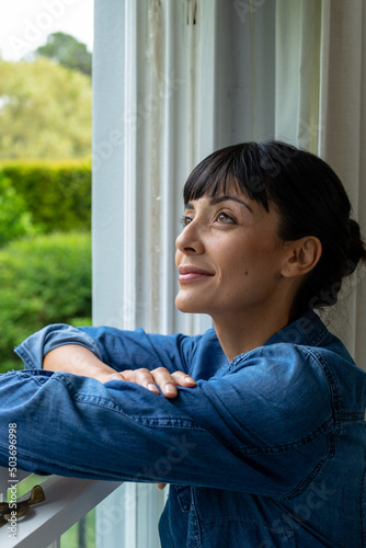 Smiling thoughtful caucasian young woman with arms crossed looking through window
