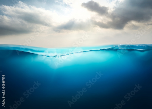 Sunlight shining through the surface of the blue ocean, sea, with a cloudy sky above and dark waters below.