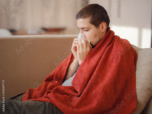 Coronavirus. Sick man of corona virus lying down in sofa and recovery from illness in home. Blowing his nose. The concept of high temperatures. The person is seriously ill.