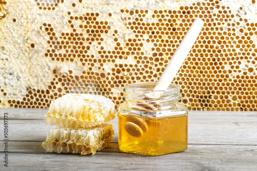 Photo jar of fresh honey and honeycombs on gray table near frame with honeycombs
