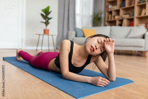Tired young asian lady wiping her forehead while lying on sports mat, exhausted from home training, copy space
