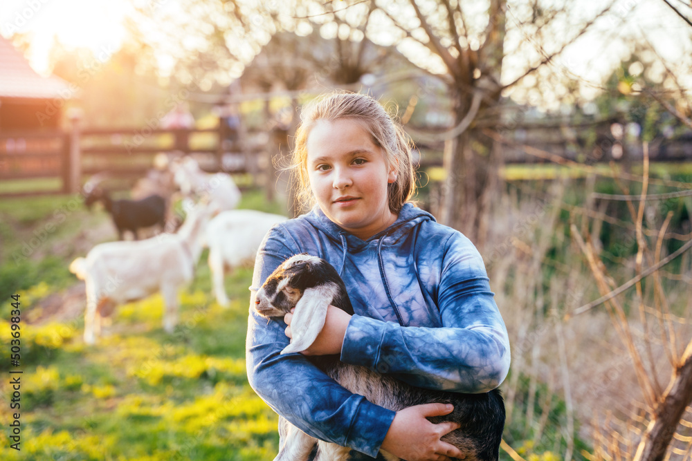 Portrait of cute teenager girl with holding goat kid domestic animal at farm in countryside. Agritourism concept.