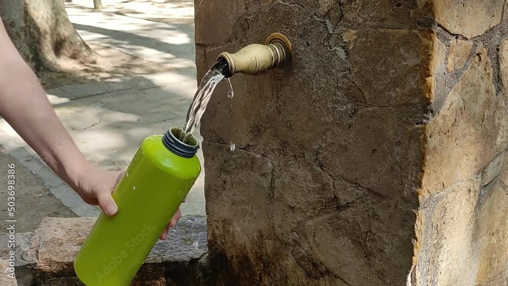 Rellenando botella de agua o cantimplora en fuente pública de agua potable
