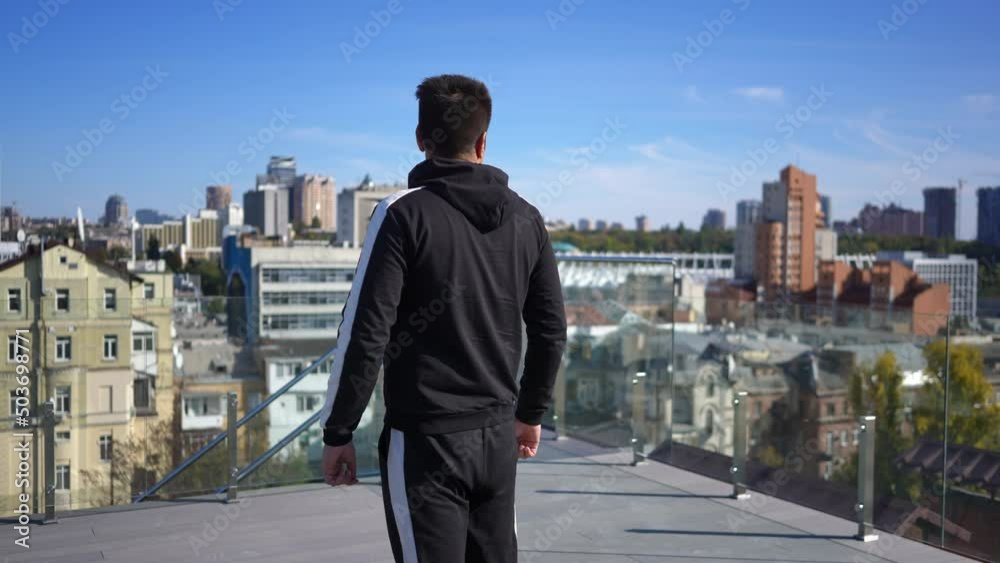 Tracking shot of confident Middle Eastern man walking on rooftop on sunny day in Kyiv Ukraine looking around stretching. Young millennial guy enjoying summer spring morning outdoors Tracking shot of confident Middle Eastern man walking on rooftop on sunny day in Kyiv Ukraine looking around stretching. Young millennial guy enjoying summer spring morning outdoors