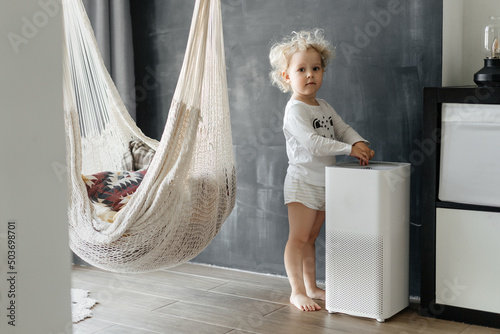 A small child with blond curly hair is enjoying fresh clean air from a dust cleaning system at home. Technology and human health. photo