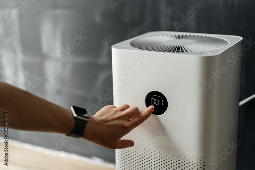 woman's hand presses the touch screen button to start an air purifier in her apartment. Human Health and Technology. photo