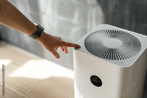 A woman's hand presses the start button of an air purifier in her apartment. Health and technology. photo