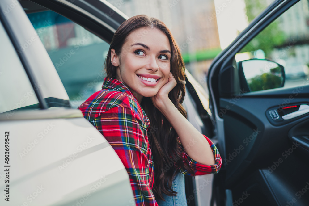 Portrait of attractive cheerful wavy-haired girl passenger sitting in auto waiting husband shopping on parking outdoors