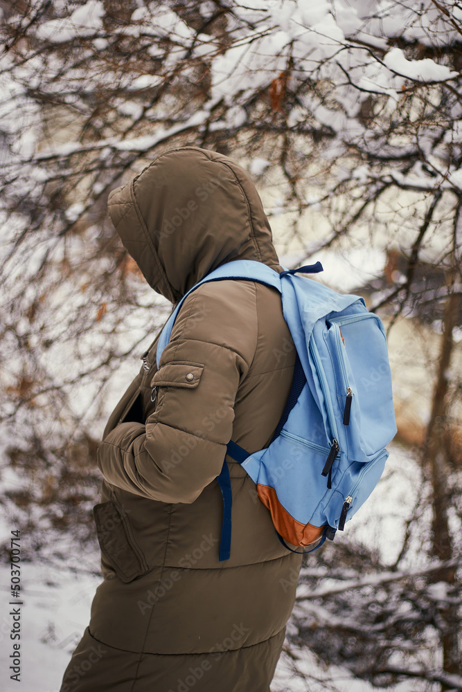 A woman in winter clothes and with a blue backpack walks among the snow-covered trees. Winter season in the woods. 