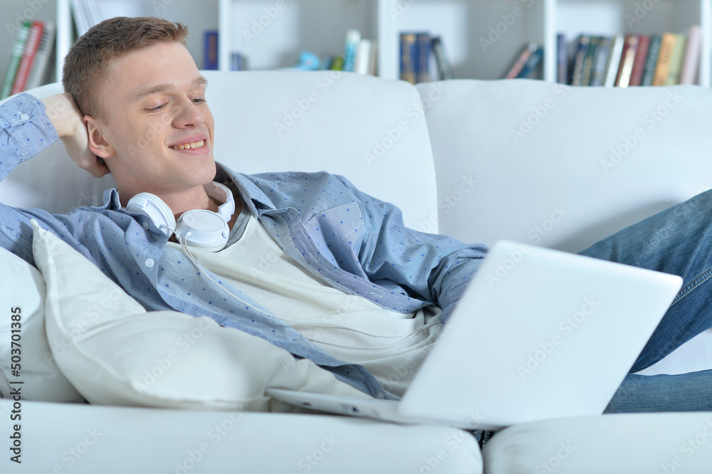 handsome young man lying on white couch with laptop handsome young man lying on white couch with laptop