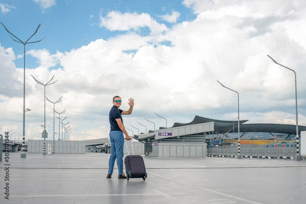 A man with a suitcase in an airport parking lot waving. A man with a suitcase in an airport parking lot waving.