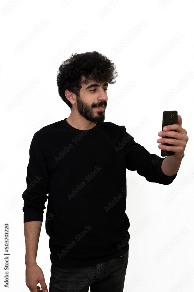 Curly haired young male in black sweater looking at mobile phone smiling. Isolated on white background Curly haired young male in black sweater looking at mobile phone smiling. Isolated on white background