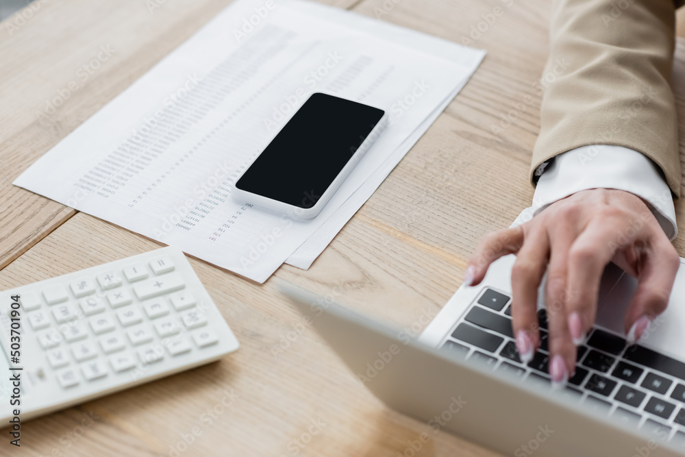 cropped view of accountant typing on laptop near smartphone, calculator and documents. cropped view of accountant typing on laptop near smartphone, calculator and documents.