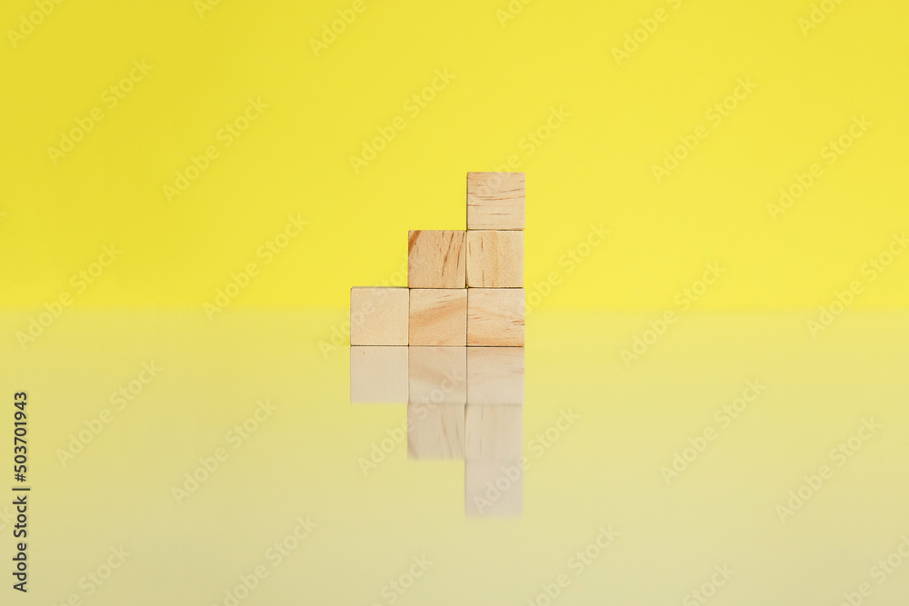 Wooden cubes together arranged in column on yellow background with reflection. Conceptual and symbolic image. Copy space. Wooden cubes together arranged in column on yellow background with reflection. Conceptual and symbolic image. Copy space.