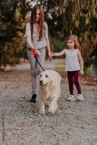 Two little girls sisters walking outside with white fluffy dog in the park. Beautiful countryside life