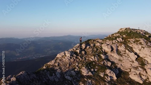 aerial orbital video footage of a man reaching on the summit of a mountain at sunset photo