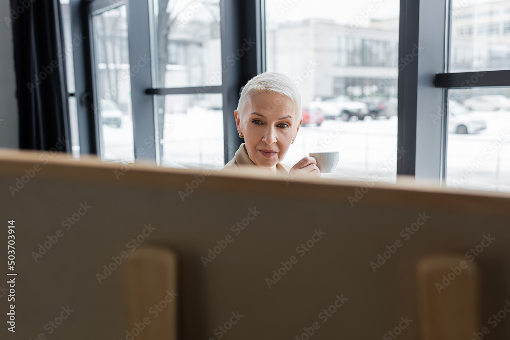 senior banker with short hair holding coffee cup near blurred flip chart. senior banker with short hair holding coffee cup near blurred flip chart.
