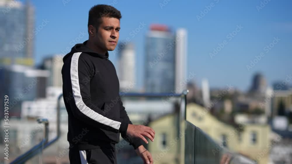 Side view Middle Eastern man walking in slow motion to glass fence on rooftop admiring sunny summer spring Kyiv Ukraine. Confident young millennial tourist enjoying journey on sunny day Side view Middle Eastern man walking in slow motion to glass fence on rooftop admiring sunny summer spring Kyiv Ukraine. Confident young millennial tourist enjoying journey on sunny day