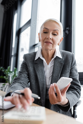accountant holding mobile phone while using blurred calculator in office. Free Download accountant holding mobile phone while using blurred calculator in office. - GFXLoad