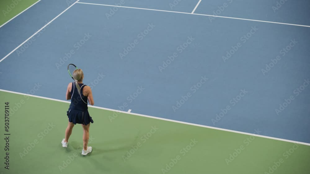 Female Tennis Player Servers by Hitting Ball with a Racquet During Championship Match. Professional Woman Athlete Strikes Successfully. World Sports Tournament. Slow Motion High Angle Wide Shot Female Tennis Player Servers by Hitting Ball with a Racquet During Championship Match. Professional Woman Athlete Strikes Successfully. World Sports Tournament. Slow Motion High Angle Wide Shot