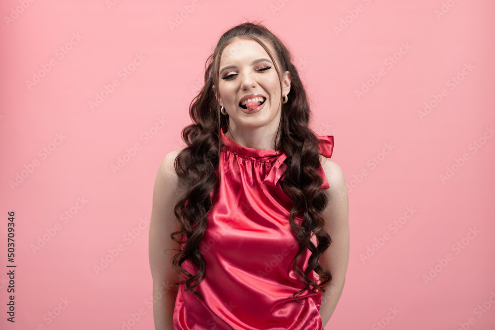 Cheerful girl with curly hair fooling around sticking her tongue out, silly face, jokes, laughing, nerdy girl on pink studio background. Cheerful girl with curly hair fooling around sticking her tongue out, silly face, jokes, laughing, nerdy girl on pink studio background.