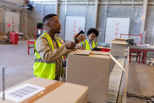 African american young man with young female coworker packaging cardboard box with adhesive tape photo