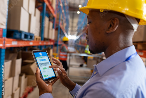 Close-up of african american young male worker tracking shipment over digital tablet in warehouse photo