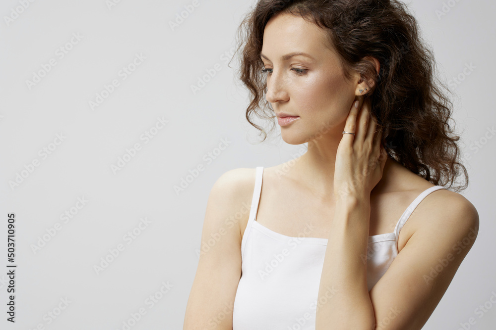 Thoughtful pensive upset curly beautiful woman in basic white t-shirt touches neck looks aside think about work posing isolated on over white background. People Emotions Lifestyle concept. Copy space Thoughtful pensive upset curly beautiful woman in basic white t-shirt touches neck looks aside think about work posing isolated on over white background. People Emotions Lifestyle concept. Copy space