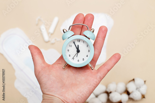 Women's hygiene pads with tampons and alarm clock on beige background photo