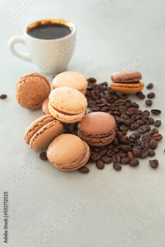 Chocolate hazelnut macarons with coffee beans and a coffee cup on a gray background with copy space. Vertical photo with confectionery - macaron.