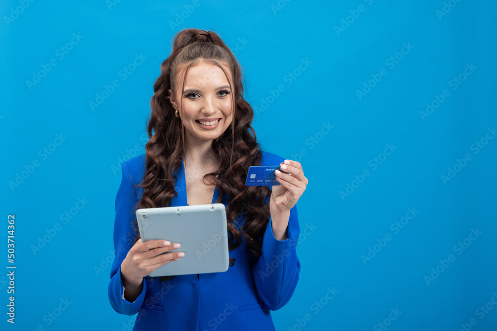 Portrait of young smiling brunette showing credit card holding tablet, online banking, easy payments, blue background. Portrait of young smiling brunette showing credit card holding tablet, online banking, easy payments, blue background.