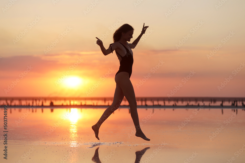silhouette of a young slim woman in a swimsuit who dancing at sunset on the sea. summer holiday silhouette of a young slim woman in a swimsuit who dancing at sunset on the sea. summer holiday