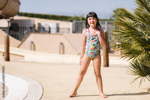 Happy little kid in swimwear standing near pool on sunny day photo