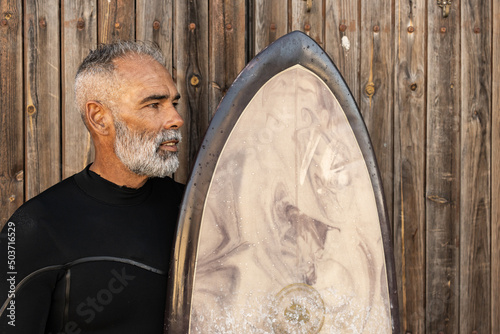 Canvas Print A middle-aged African man in a surfing costume holding his surfing board and loo