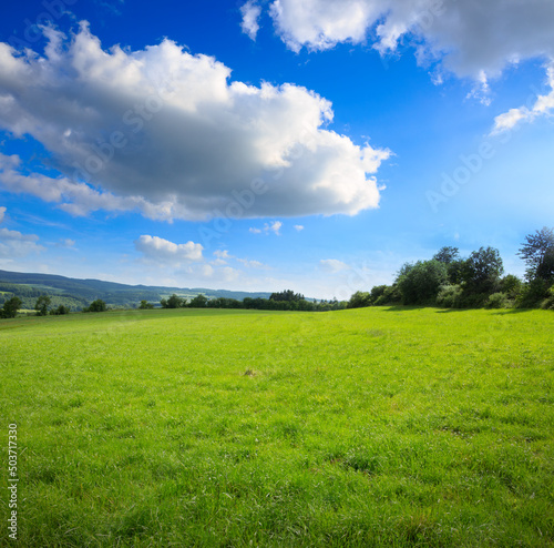 Spring field and blue sky with big clouds and sunlight.