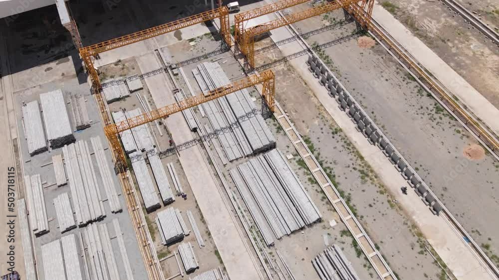 Top view of concrete pillar stacks laying on the ground in front of large warehouse construction site. Construction materials. Infrastructure themes. Top view of concrete pillar stacks laying on the ground in front of large warehouse construction site. Construction materials. Infrastructure themes.