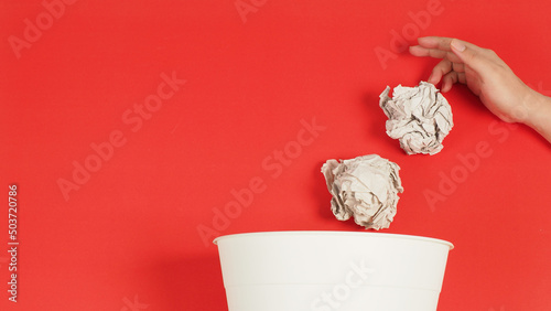 The crumpled white paper is mauled with thand and a trash can on red background. photo