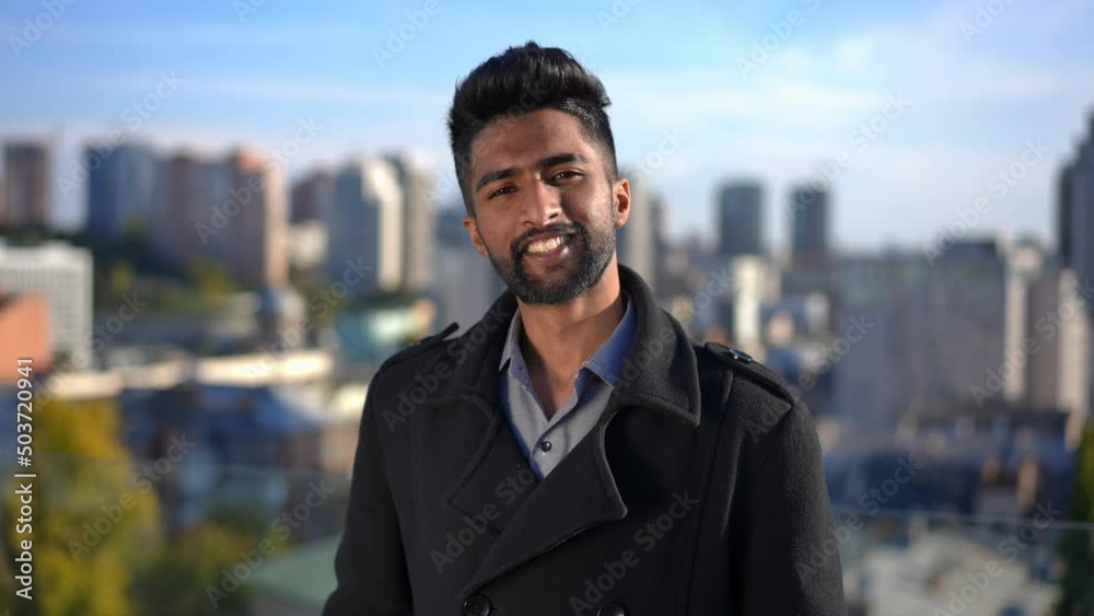Young confident man with toothy smile looking at camera posing in sunbeam outdoors. Portrait of Middle Eastern handsome guy looking at camera smiling with Kyiv Ukraine at background Young confident man with toothy smile looking at camera posing in sunbeam outdoors. Portrait of Middle Eastern handsome guy looking at camera smiling with Kyiv Ukraine at background