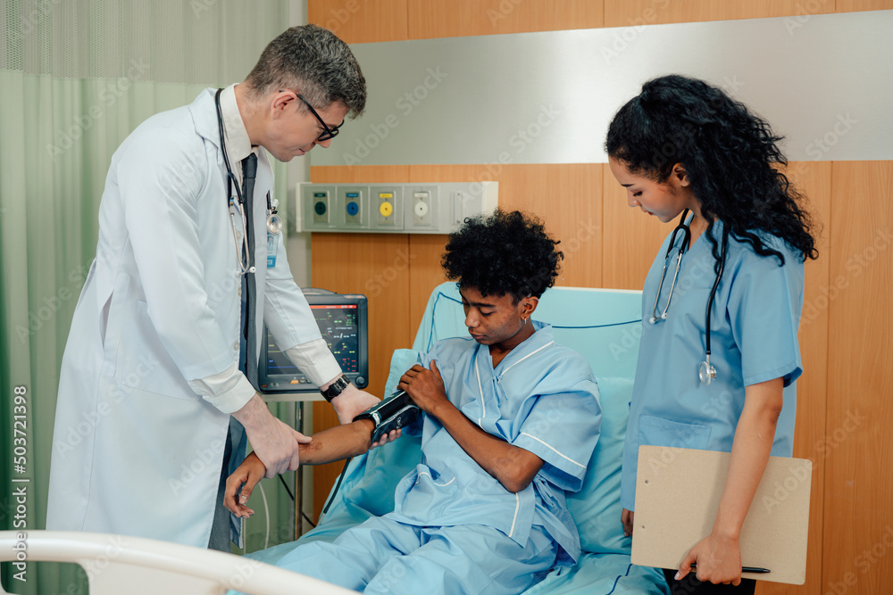 Young patient man sitting in bed while doctor checking his pulse. Doctor examining senior male patient in hospital room. Young patient man sitting in bed while doctor checking his pulse. Doctor examining senior male patient in hospital room.