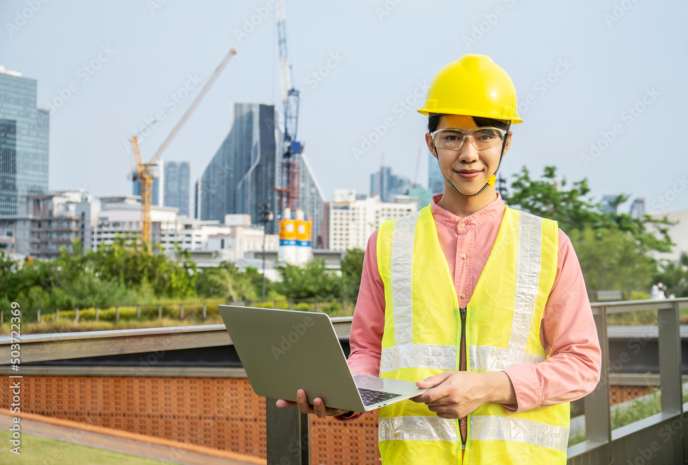 Engineer or construction worker Asian man is holding the laptop and working concentrated at building plan, Hard hat help protect with operation Engineer or construction worker Asian man is holding the laptop and working concentrated at building plan, Hard hat help protect with operation
